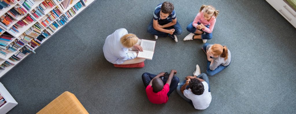 Kinder sitzen im Kreis, ein Erwachsener liest vor
