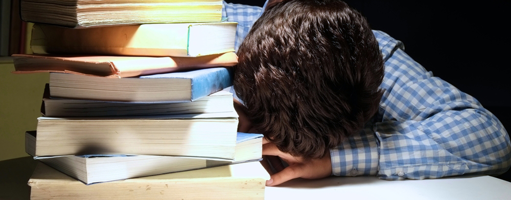 Ein Junge legt seinen Kopf auf einen Tisch voller Bücher